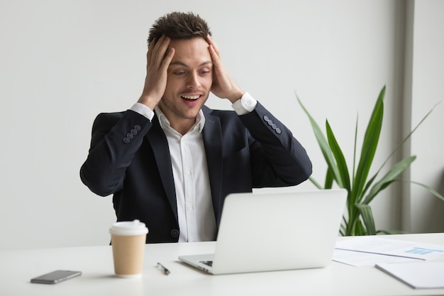 Emocionado hombre de negocios del milenio sorprendido por inesperadas buenas noticias en línea