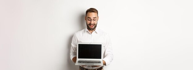 Emocionado hombre de negocios mostrando algo en la pantalla del portátil de pie feliz sobre fondo blanco.