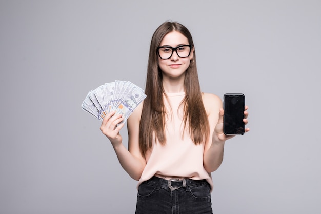 Emocionado joven estadounidense con abanico de billetes de un dólar y plata celular aislado sobre pared blanca