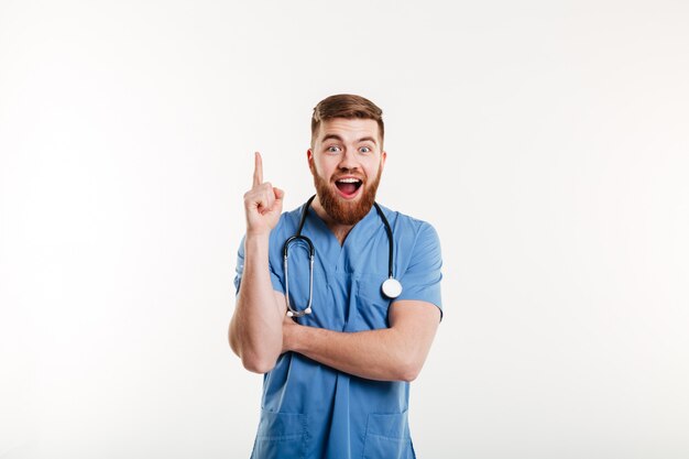 Emocionado joven médico masculino apuntando el dedo hacia arriba en copyspace