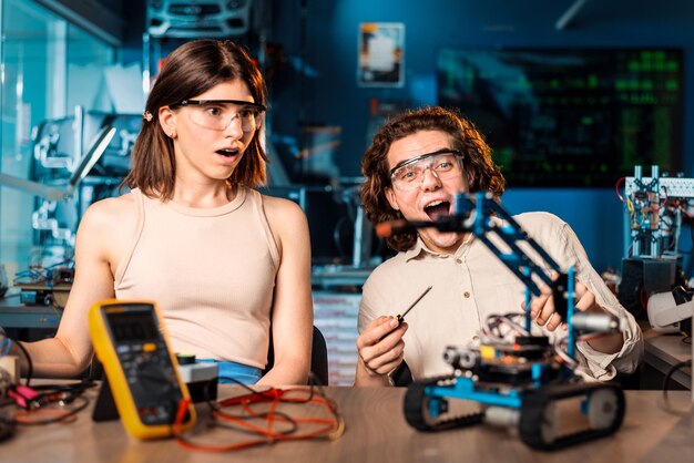 Emocionado joven y mujer con gafas protectoras haciendo experimentos en robótica en un laboratorio