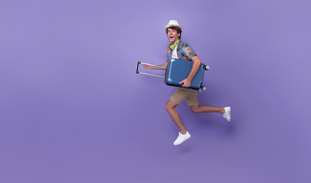 Emocionado joven turista feliz con equipaje saltando aislado sobre fondo de estudio púrpura