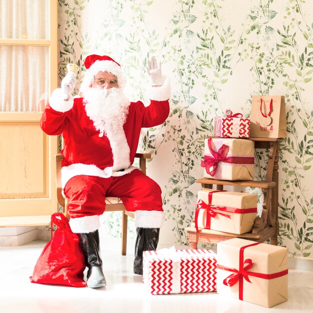 Emocionado Santa Claus sentado en la silla junto a los regalos
