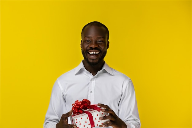 Emocionado sonriente joven barbudo afroamericano sostiene un regalo en dos manos y mira delante de él