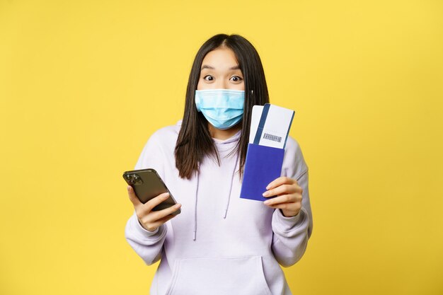 Emocionado turista mujer asiática mostrando pasaporte y boletos usando la aplicación de teléfono inteligente yendo de vacaciones stan ...