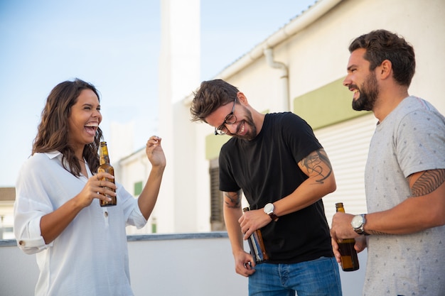 Emocionados amigos felices bebiendo cerveza, charlando y riendo