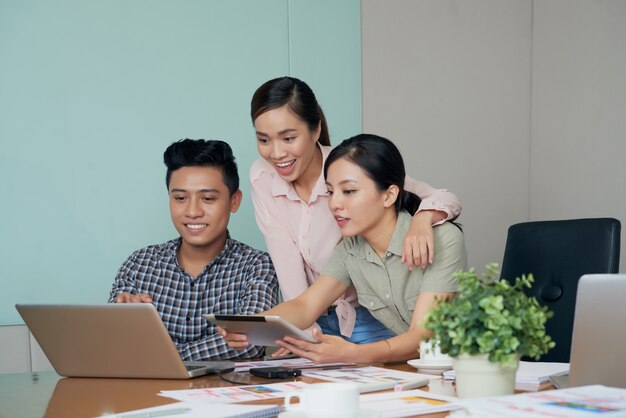 Emocionados colegas asiáticos mirando la pantalla del portátil juntos en la oficina