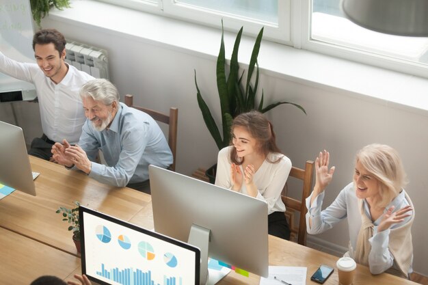 Emocionados motivados, jóvenes y viejos colegas que aplauden celebrando el éxito corporativo.