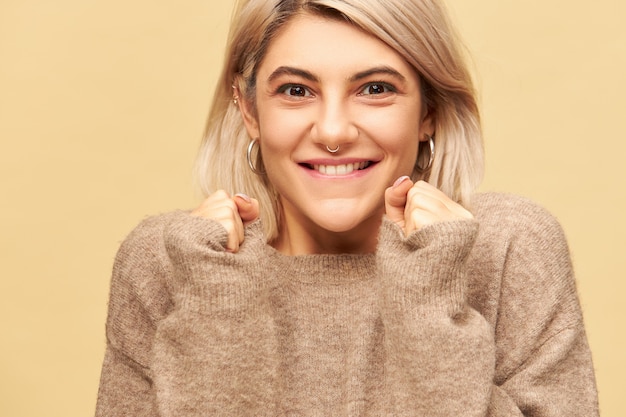 Emocional eufórica mujer joven linda con peinado bob rubio y anillo en la nariz exclamando con entusiasmo, con una mirada llena de alegría, animando, regocijándose por el éxito, mirando con una amplia sonrisa radiante, mordiendo el labio