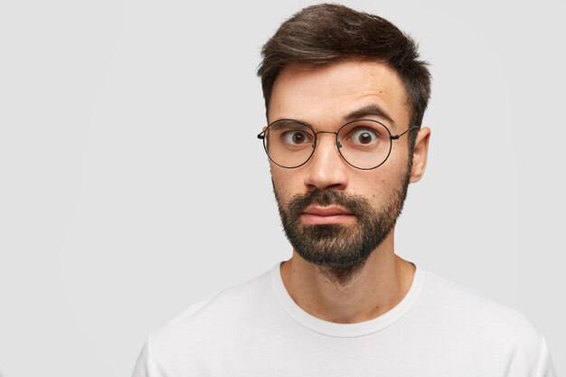 Emocional joven barbudo con barba densa, peinado de moda, mira con sorpresa