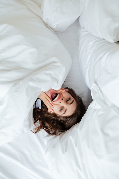 Foto gratuita emocional joven se encuentra en la cama en su casa debajo de una manta