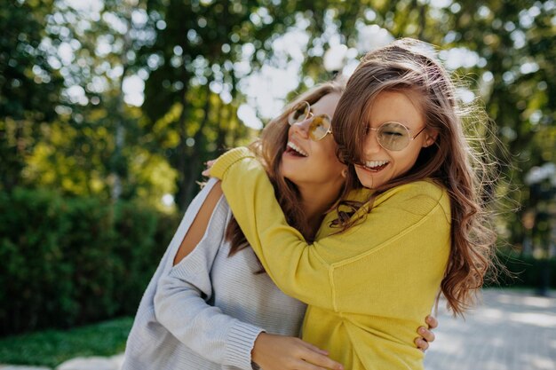 Emocionales dos chicas adorables se abrazan y sonríen mientras pasan tiempo afuera en un cálido día de verano