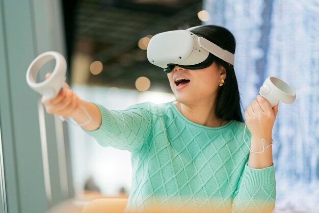Emocionante jugadora asiática jugando juegos 3d futuristas de metaverso aumentado de realidad virtual en el restaurante del café Hermosa mujer joven jugando en gafas de realidad virtual con diversión y alegría