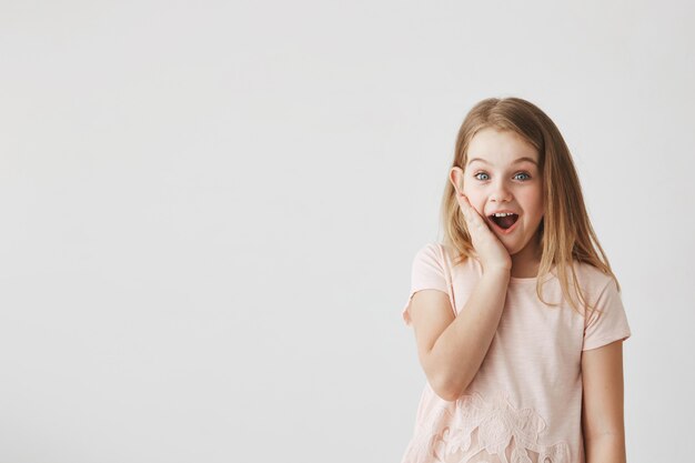 Emociones y expresiones positivas. Niña linda con expresión feliz y emocionada, de la mano en la mejilla, sorprendiéndose al recibir flores del niño.