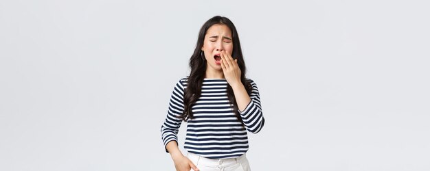 Emociones de la gente de estilo de vida y concepto casual Mujer cansada y soñolienta que trabaja hasta tarde en la oficina cierra los ojos y bosteza quiere ir mal La niña asiática se despertó temprano necesita un puesto de café fondo blanco