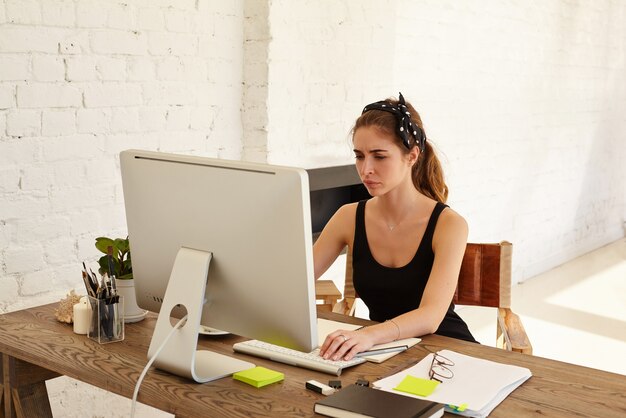 Emociones humanas negativas. La mujer molesta mira la pantalla trabajando en un escritorio frente a la computadora en la oficina moderna. Diseñador o arquitecto cansado que trabaja en el escritorio