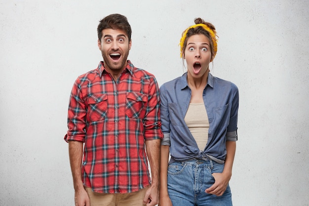 Foto gratuita emociones humanas positivas, sentimientos, actitud y concepto de reacción. retrato de hombre barbudo joven sorprendido en camisa a cuadros roja y mujer con diadema posando