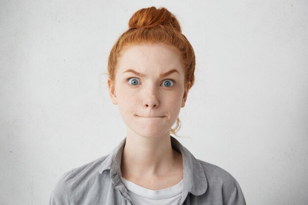 Emociones humanas, sentimientos, percepción de la vida, reacción y actitud. Mujer joven pelirroja nerviosa asustada levantando las cejas y persiguiendo los labios, manteniendo el secreto, se supone que no debe decirle nada a nadie