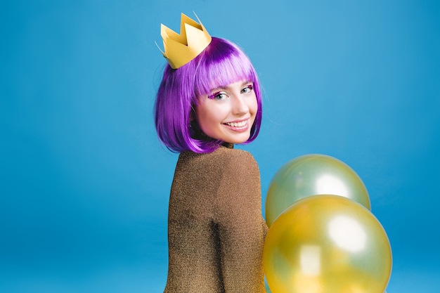 Emociones positivas brillantes de alegre joven con corte de pelo púrpura celebrando la fiesta con globos. Corona de oro, humor alegre, celebración de fiestas, cumpleaños.
