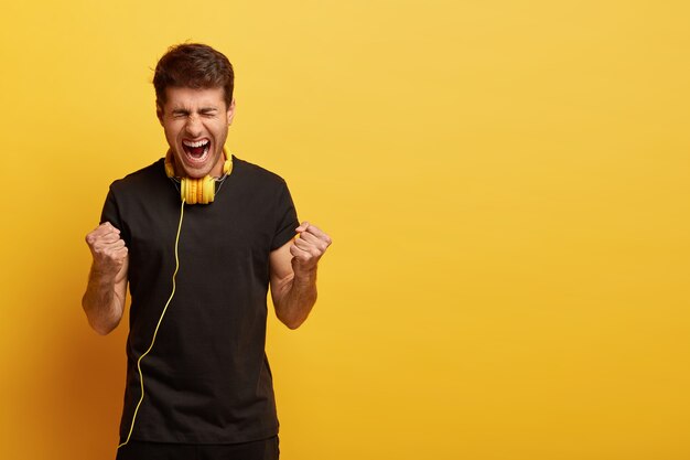 Emotivo hombre europeo con cabello oscuro, viste camiseta negra, no puede imaginar la vida sin música