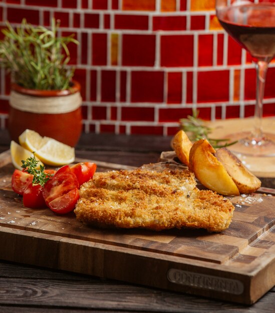 Empanadas de pollo fritas servidas con papas fritas, limón y tomate sobre tabla de madera