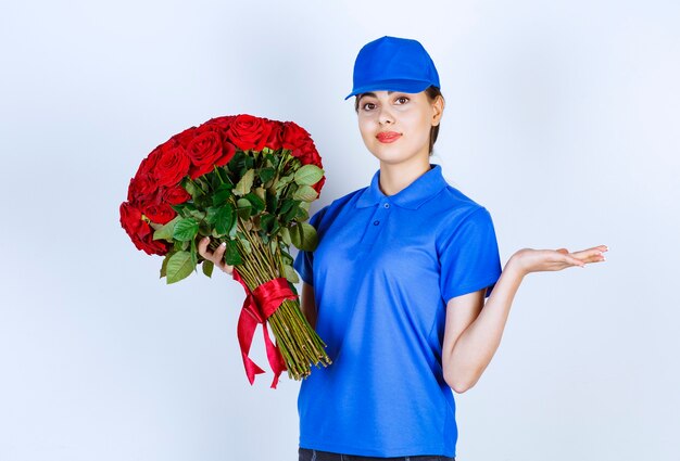 Empleada de entrega en uniforme azul de pie y sosteniendo un ramo de rosas.