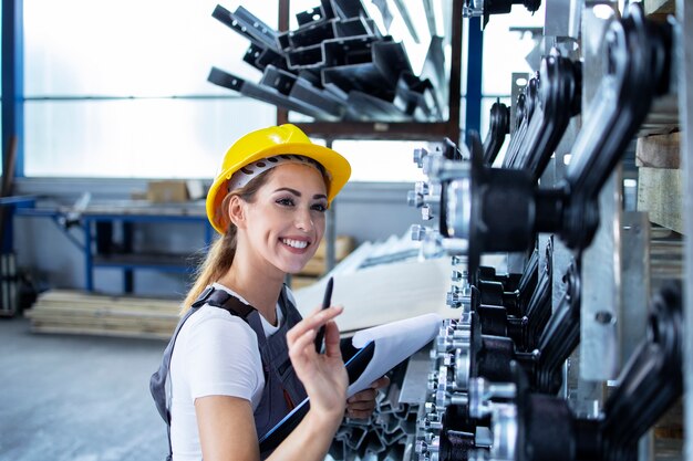 Empleada industrial femenina en uniforme de trabajo y casco comprobando la producción en la fábrica.