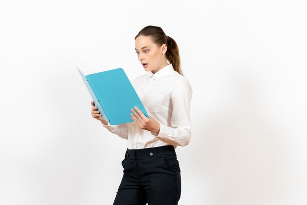 Empleada de oficina en blusa blanca sosteniendo y leyendo archivo azul sobre blanco claro