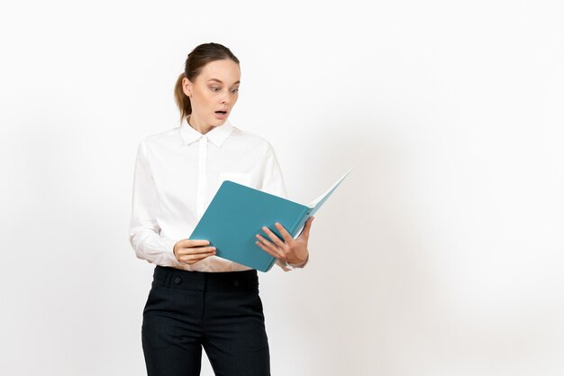 Empleada de oficina en blusa blanca sosteniendo y leyendo archivo azul sobre blanco claro