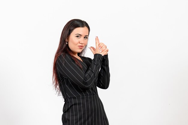 Empleada de oficina en estricto traje negro en pose de pistola sosteniendo en blanco
