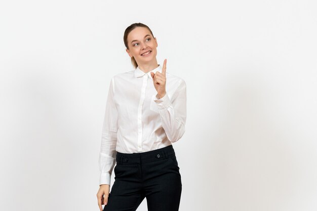 Empleada de oficina posando y levantando su dedo en blusa blanca sobre blanco