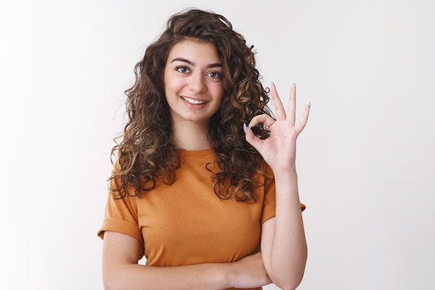 Empleado armenio joven apuesto profesional determinado que muestra el gesto bien entendido la tarea, hace el gesto correcto sonriendo ampliamente de acuerdo piensa que el atuendo se ve excelente, de pie fondo blanco