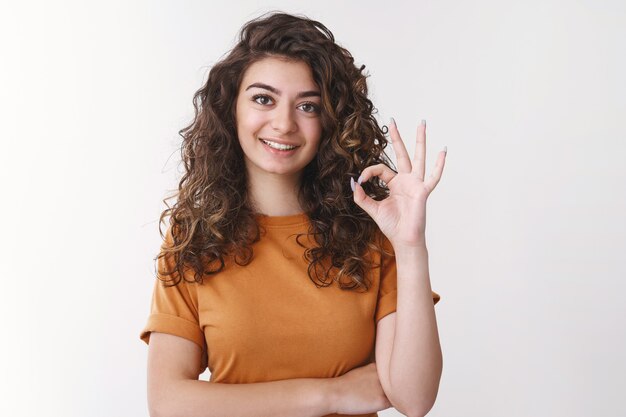 Empleado armenio joven apuesto profesional determinado que muestra el gesto bien entendido la tarea, hace el gesto correcto sonriendo ampliamente de acuerdo piensa que el atuendo se ve excelente, de pie fondo blanco