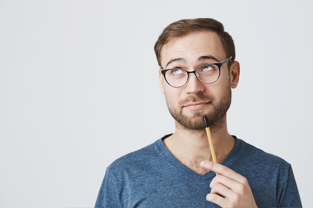 Empleado barbudo en gafas, sosteniendo el lápiz, mirar hacia otro lado reflexionando