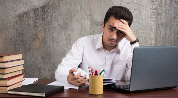 Empleado cansado sentado en el escritorio y mirando hojas de papel. Foto de alta calidad