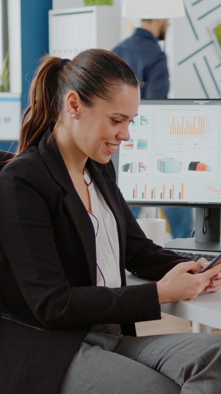 Foto gratuito empleado corporativo mirando la pantalla del teléfono inteligente mientras trabaja en la planificación empresarial con computadora y gráficos en la oficina de la empresa. empresaria que usa el teléfono móvil para intercambiar ideas
