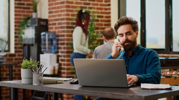 Empleado de la empresa que responde a una llamada telefónica fija en un trabajo corporativo, hablando con el gerente en la línea telefónica del cable de la oficina. Tener una conversación remota con el número de teléfono en el trabajo, llamada de negocios.