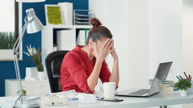 Empleado estresado cometiendo errores en el trabajo de inicio de la oficina, usando estadísticas de ventas para hacer investigación de datos. Mujer decepcionada que se siente disgustada con el fracaso de la empresa comercial, trabajando en una laptop.