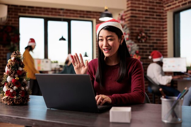 Empleado de inicio hablando en una videollamada en una oficina festiva, reuniéndose en un chat de videoconferencia en línea en un espacio decorado con adornos navideños. Mujer charlando en una llamada de teleconferencia remota.
