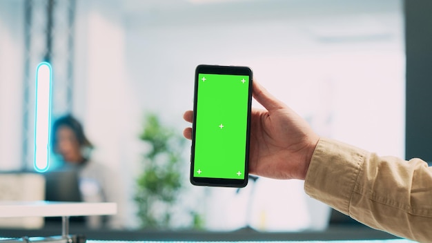 Empleado joven que usa un teléfono móvil con pantalla verde, mostrando una pantalla de espacio de copia aislada en el teléfono inteligente. Asistente de tienda masculino con plantilla de maqueta de clave de croma en blanco en boutique. De cerca.