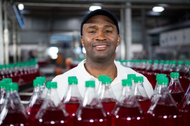 Empleado masculino sonriente de pie junto a botellas de jugo en la fábrica.