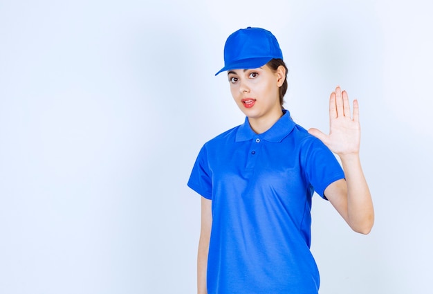 Empleado de la mujer de entrega en uniforme azul de pie y mostrando la señal de stop.