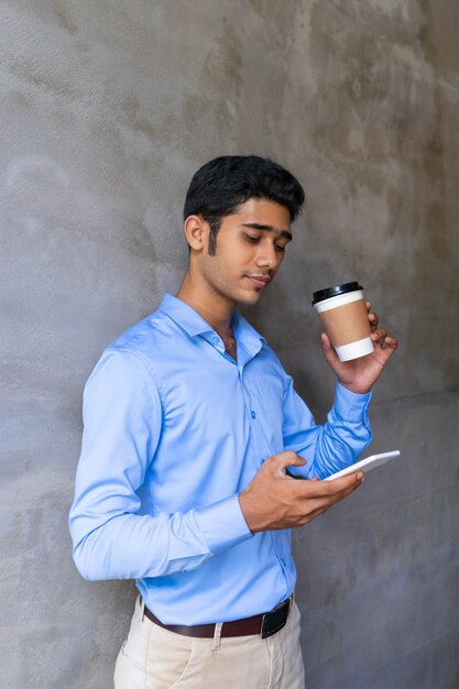 Empleado de oficina joven enfocado que charla en el teléfono móvil durante descanso para tomar café.