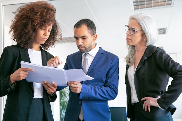 Empleadores de oficina confiados que controlan documentos juntos. Tres trabajadores profesionales enfocados sosteniendo papeles y firmando informes estadísticos en la sala de reuniones. Concepto de trabajo en equipo, negocios y gestión