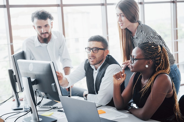 Empleados jóvenes sentados en la oficina en la mesa y usando una computadora portátil, un concepto de reunión de lluvia de ideas de trabajo en equipo.