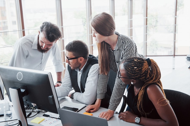 Empleados jóvenes sentados en la oficina en la mesa y usando una computadora portátil, un concepto de reunión de lluvia de ideas de trabajo en equipo.