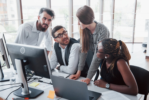 Empleados jóvenes sentados en la oficina en la mesa y usando una computadora portátil, un concepto de reunión de lluvia de ideas de trabajo en equipo.