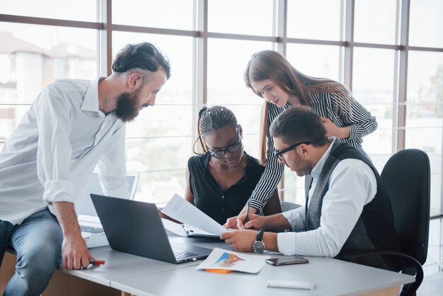 Empleados jóvenes sentados en la oficina en la mesa y usando una computadora portátil