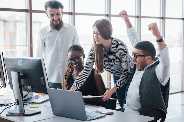 Empleados jóvenes sentados en la oficina en la mesa y usando una computadora portátil