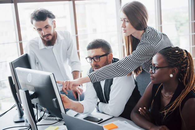 Empleados jóvenes sentados en la oficina en la mesa y usando una computadora portátil